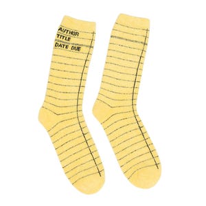 May include: A pair of yellow socks with a lined paper design. The socks have black horizontal lines and vertical lines on the sides. The top of the socks have the words "AUTHOR", "TITLE", and "DATE DUE" printed in black.