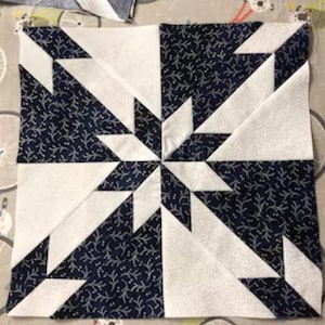 May include: A white and navy blue quilt block with a starburst pattern. The fabric has a small white floral design on a navy blue background.