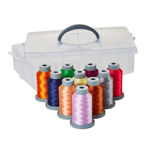 Puede incluir: Una caja de almacenamiento de plástico transparente con asa, que contiene 10 carretes de hilo de bordar de colores. Los carretes están dispuestos en círculo, con colores de hilo que incluyen naranja, rojo, verde, azul, morado y amarillo.