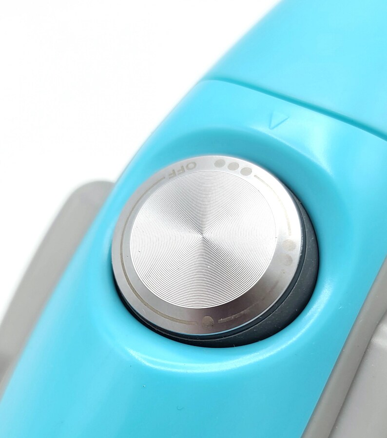 Puede incluir: Primer plano de un cepillo de dientes el&eacute;ctrico azul claro con un bot&oacute;n de encendido plateado etiquetado como "OFF".