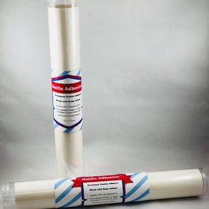 May include: Two rolls of white adhesive backed fabric. The label on the roll reads "Hotfix Adhesive, Permanent Flexible Adhesive, Works with Home Iron, Apply with a household iron, Once applied it is washable and dry cleanable, 12" x 1 Yard".