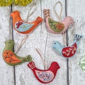 May include: Five felt bird ornaments with embroidered details. The birds are in shades of orange, green, pink, red, and blue. Each bird has a loop for hanging.
