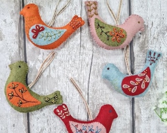 Puede incluir: Cinco adornos de pájaros de fieltro con detalles bordados. Los pájaros son en tonos naranja, verde, rosa, rojo y azul. Cada pájaro tiene un lazo para colgar.