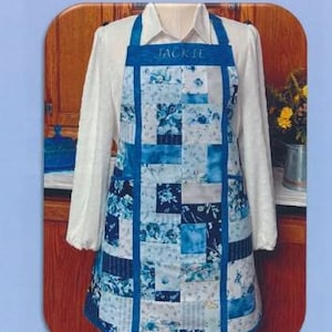 Pode incluir: Um avental de patchwork azul e branco com o nome "Jackie" bordado na frente. O avental é feito em peças e forrado com bolsos.
