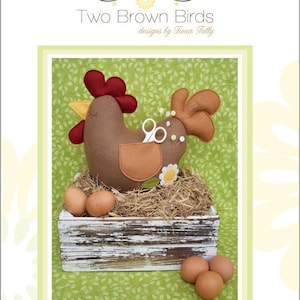 Puede incluir: Una gallina de fieltro con cresta roja, cuerpo marrón y bolsillo marrón, sentada en un nido en una caja de madera blanca. La imagen incluye huevos y el texto "Two Brown Birds" y "Henrietta".