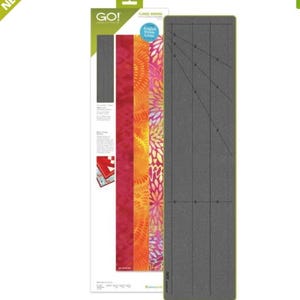 Puede incluir: Una estera de corte gris con líneas anguladas y marcas para acolchar. La estera está etiquetada como "GO!" y "Flange Binding".