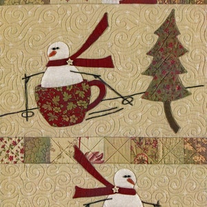 Puede incluir: Dos mu&ntilde;ecos de nieve en tazas rojas con bufandas rojas est&aacute;n esquiando cuesta abajo. El fondo es una tela beige con un patr&oacute;n acolchado.