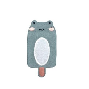 May include: A gray felt frog-shaped ice cream patch with a white belly and a pink stick.