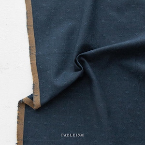 May include: A close-up of navy blue fabric with a cross pattern. The edge of the fabric has a brown border. The word "FABLEISM" is printed in white at the bottom of the image.