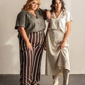 Op de afbeelding: Twee vrouwen modelleren een shirtpatroon genaamd "The Donny Shirt" van FRIDAY pattern co. Het patroon is voor geweven stoffen en is verkrijgbaar in de maten XS-7X. Het shirt is een overhemd met een kraag en een V-hals. Een vrouw draagt een groen shirt met zwart-wit gestreepte broek. De andere vrouw draagt een wit shirt met een rok met bloemenprint.