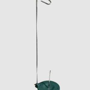 May include: A metal thread stand with a green base and a hook at the top. The stand is used to hold thread while sewing.