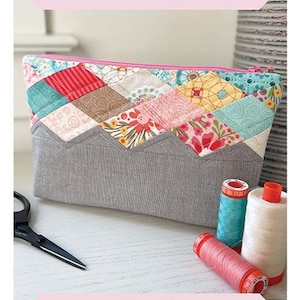 Op de afbeelding: Een patchwork Paragon Pouch met een roze rits, met een grijze basis en een kleurrijke bovenkant met bloemen- en geometrische patronen. De afmeting is 15 cm x 23 cm x 5 cm. De tekst "Paragon Pouch" wordt bovenaan weergegeven.