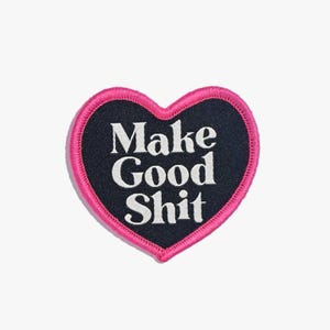 Puede incluir: Un parche en forma de corazón rosa con tela negra y texto blanco que dice "Make Good Shit".