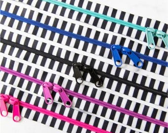 May include: A selection of colourful zippers, including teal, blue, black, purple, and pink, arranged on a black and white striped fabric. The image highlights the different colours and the details of the zipper mechanisms.
