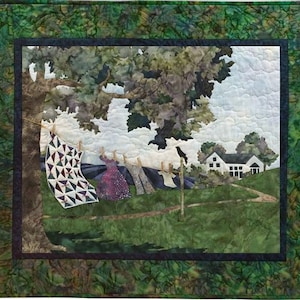May include: A quilted wall hanging depicting a rural scene. A clothesline with hanging laundry is in the foreground, with a house and trees in the background. The quilt has a green border and a detailed, colorful design.
