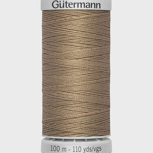 May include: A spool of Gütermann thread in a light brown color. The spool has a white top and bottom with the brand name printed on the top. The bottom of the spool reads "100 m - 110 yds/vgs".