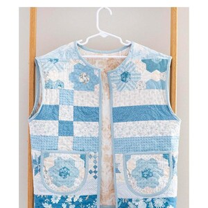 May include: A quilted vest pattern in shades of blue and white, displayed on a hanger. The vest features floral and geometric patterns, with the text "Quilter's Vest" and "Quilted Vest Pattern" at the top. The Laundry Basket Quilts logo is also visible.