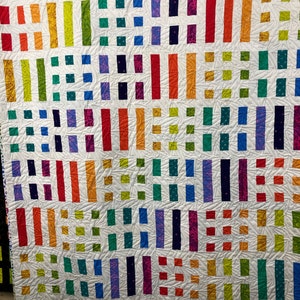 Puede incluir: Una colcha colorida con fondo blanco. La colcha está hecha de filas de tiras de tela de diferentes colores y cuadrados. Las tiras de tela están dispuestas en un patrón vertical, mientras que los cuadrados están dispuestos en un patrón horizontal. La colcha es una obra de arte vibrante y llamativa.