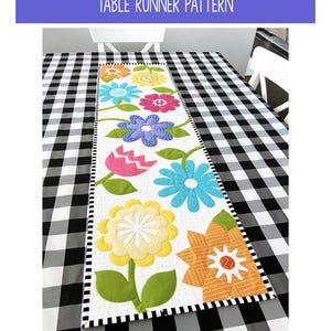 Op de afbeelding: Een bloemenpatroon voor een tafelloper met de tekst "Flower Garden" en "Table Runner Pattern". De afmeting is 30 cm x 107 cm. De loper heeft verschillende bloemontwerpen in heldere kleuren op een witte achtergrond.