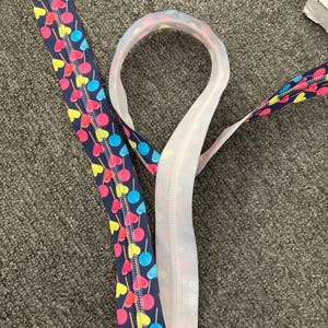 Könnte beinhalten: Ein farbenfroher Reißverschluss mit einem marineblauen Stoff, der ein Muster aus Herzen und Kreisen in Gelb, Rosa und Blau aufweist. Das Reißverschlussband ist weiß.
