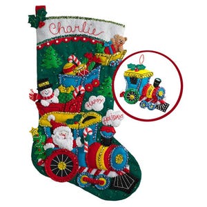 May include: A festive Christmas stocking with a train design, featuring Santa Claus, a snowman, and the name "Charlie." The stocking is green, red, blue, and yellow, with "Happy Holidays." An ornament of a train is also included.