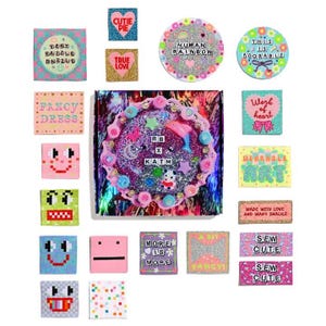 May include: A collection of colourful, glittery, and patterned iron-on patches with various phrases and designs, including "Cutie Pie", "True Love", "Human Rainbow", "This is Adorable", "Fancy Dress", "Work of Heart", "Wearable Art", "More is More", "A Bit Fancy", "Sew Cute", and "RB x KATM".
