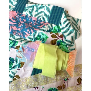 Puede incluir: Una colección de retazos de tela coloridos con estampados florales y geométricos. Una cinta verde neón está enrollada junto a un adorno transparente en forma de pez con aletas naranjas. Las telas incluyen tonos de azul, rosa y verde.