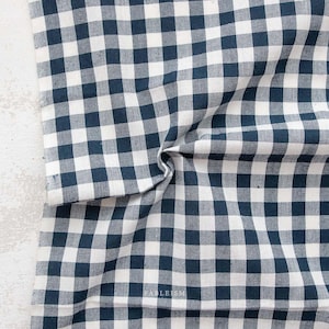 May include: A white and navy blue gingham fabric with a checkered pattern. The fabric is folded in half and has a slight wrinkle.