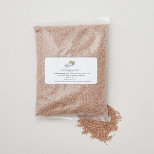 May include: A clear plastic bag filled with ground black walnut shells. The bag has a white label with text that reads "Ground Black Walnut Shells" and a warning about human consumption. The product is made in the USA.