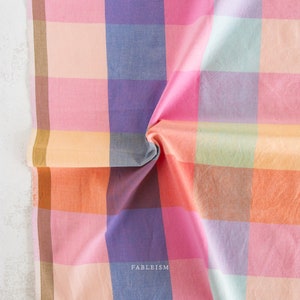 Può includere: Un tessuto a quadri colorato con una varietà di colori pastello, tra cui rosa, arancione, blu e verde. Il tessuto è piegato in modo da mostrare i diversi colori e motivi.