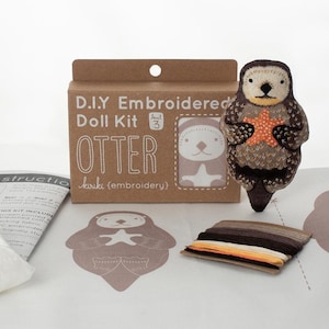 Puede incluir: Kit de muñeca bordada DIY: Nutria, un kit de manualidades con una nutria marrón y blanca sosteniendo una estrella de mar. El kit incluye hilo de bordar, tela e instrucciones.