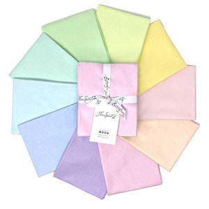 Puede incluir: Un conjunto de diez cuadrados de tela de 45,7 cm por 55,9 cm en colores pastel, incluyendo azul claro, lavanda, rosa, amarillo y verde. Los cuadrados de tela están dispuestos en círculo y atados con una cinta. La cinta tiene una etiqueta que dice "Free Spirit".