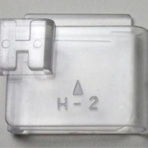 Könnte beinhalten: Eine transparente Kunststoffkomponente mit einem "H"-förmigen Clip und dem Text "H-2". Die Komponente hat einen rechteckigen Körper mit leicht abgerundeter Oberseite und einem kleinen Dreieckssymbol.