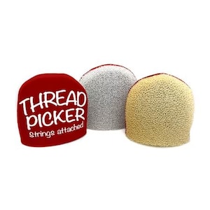 May include: Three thread pickers in a row. The first is red with white text that reads "THREAD PICKER Strings attached". The second is gray, and the third is tan. All three have a rounded, dome-like shape.