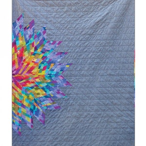 Puede incluir: Un edredón con un diseño vibrante y colorido sobre un fondo gris. El edredón presenta un gran patrón floral estilizado en tonos de rojo, amarillo, azul y morado. El texto "LUMINARY QUILT" está en la parte superior y las dimensiones son 107 cm x 140 cm.