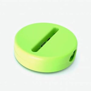 Può includere: Un organizzatore di cavi in ​​plastica verde e giallo con una fessura per tenere i cavi. L'organizzatore ha la forma di una pillola.
