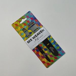 May include: MX Weaver tools by Mr. Domestic on a colourful geometric patterned card. The card has a hole for hanging and the text "For fabric weaving, reimagined." Two metal weaving tools are visible.