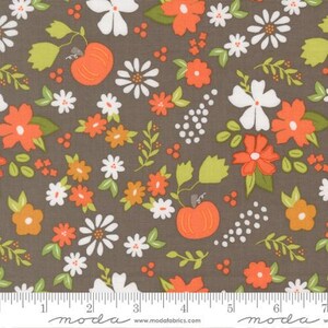 May include: A brown fabric featuring a repeating pattern of orange pumpkins, white daisies, orange flowers, and light green leaves. A white ruler is visible at the bottom edge, showing measurements in inches up to 7 inches for scale.