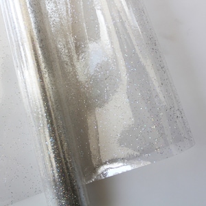 May include: Clear wrapping paper with iridescent glitter. The paper has a subtle shimmer and is perfect for adding a touch of sparkle to gifts.