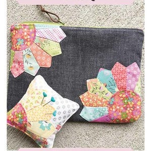 May include: A grey pouch with colourful Dresden plate patchwork accents and a matching pincushion. The pouch has a leather zipper pull and the text "Double Dresden Pouch". Finished size is 17.78 cm x 25.4 cm.