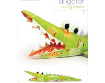 May include: A sewing pattern for a green alligator plush toy with a colorful patterned fabric. The pattern is titled "alligator sewing pattern" and is from the company "penguin & fish".