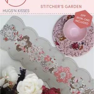 May include: A floral-patterned table runner with a scalloped edge, featuring pink, gray, and brown flower designs. The text "MAPLE SYRUP RUNNER" and "HUGS'N KISSES" are visible. A pink bowl and floral plate are also in the image.