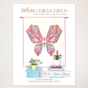Può includere: Un poster per un modello di quilt moderno intitolato "Wondergarden" di Tamara Kate. Il design presenta una farfalla geometrica in rosa, blu e motivi floreali. Il poster include il testo "Nature Study" e una citazione di W.B. Yeats.