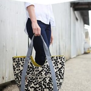 May include: A black and white tote bag with a polka dot pattern and gray straps. The bag is large and has a zippered pocket on the front. The text "POOLSIDE TOTE" and "a generous size all-purpose tote" is printed on the top of the image.