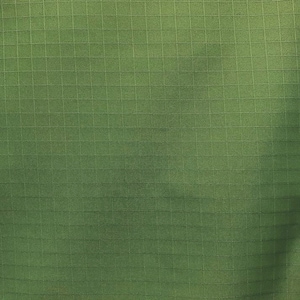 May include: A solid olive green fabric featuring a distinct grid pattern known as ripstop. The material displays a consistent square weave texture throughout the surface, characterized by a repeating series of horizontal and vertical lines.