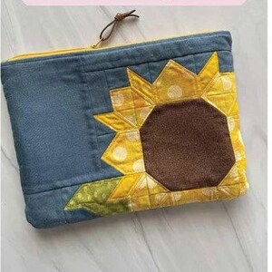May include: A blue fabric pouch with a sunflower design. The sunflower is made of yellow, brown, and white fabric. The pouch is 8 inches by 10 inches.