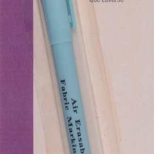 Könnte beinhalten: Hellblauer "The Fine Line" Air Erasable Stoffmarkierungsstift. Der Stift hat eine feine Spitze und erzeugt eine dünne, violette Linie, die ohne Waschen verschwindet. Die Verpackung enthält das "Fine Point"-Logo.