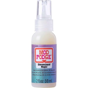 May include: A clear bottle of Mod Podge Dimensional Magic, a craft adhesive, with a white liquid and a clear spray nozzle. The label reads "Adds Iridescent Glitter 3D Accents" and contains 2 fl oz, equivalent to 59 ml.