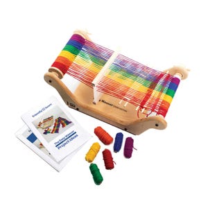 Könnte beinhalten: Ein Easy Weaver Webstuhl aus Holz mit Regenbogenfarbenem Garn. Der Webstuhl hat eine helle Holzoberfläche und ist mit bunten Fäden bestückt. Das Bild enthält auch ein Heft mit dem Titel "The Easy Weaver Project Ideas" und mehrere Garnrollen.