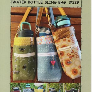 Könnte beinhalten: Drei Wasserflaschen-Umhängetaschen mit verschiedenen Stoffmustern und Farben. Die Taschen haben eine Reißverschlusstasche, verstellbare Träger und dekorative Anhänger. Der Text "SUZANNE'S ART HOUSE WATER BOTTLE SLING BAG #229" ist oben zu sehen.